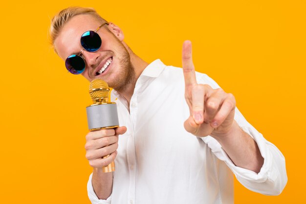 Piękny caucasian mężczyzna w szkłach śpiewa piosenki w karaoke z mikrofonem odizolowywającym na kolorze żółtym
