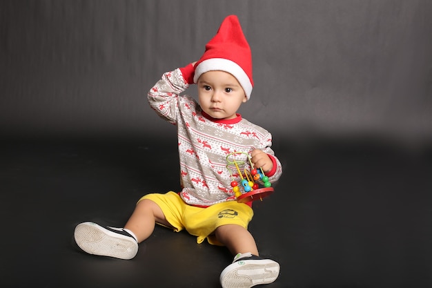 piękny chłopczyk w świątecznym swetrze Czapka Świętego Mikołaja bawi się zabawką