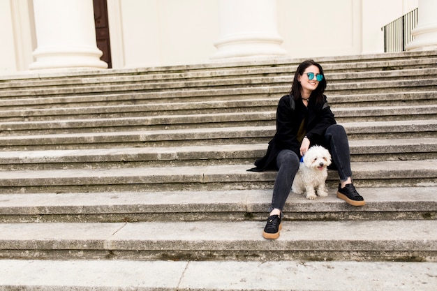 Piękny dziewczyny obsiadanie na schodkach z jej zwierzę domowe psem po spaceru w mieście
