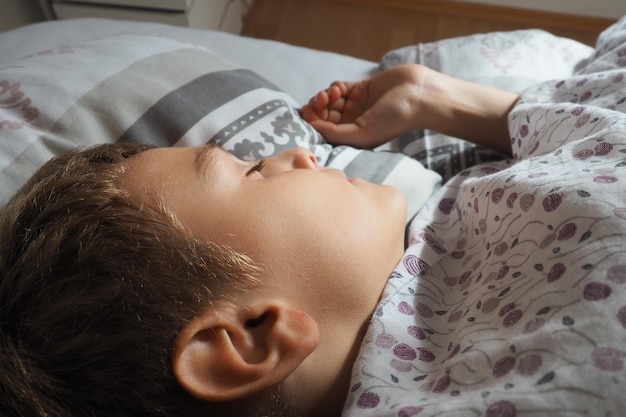 Zdjęcie piękny kaukaski chłopiec w wieku 8 lat o blond włosach śpi na łóżku z puszystym kocem i poduszką miękkie światło porannego słońca zbliżenie ucha dziecko odpoczywa zdrowy sen