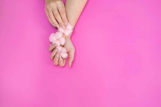Zdjęcie piękny kobiecy manicure w delikatnych odcieniach, na jasnym tle z delikatnie różowej bawełny.