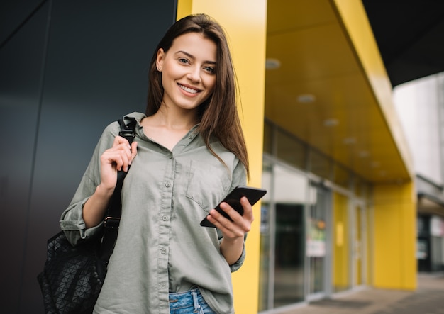 Piękny Kobiety Mienia Telefon Komórkowy, Patrzejący Kamerę, Ono Uśmiecha Się, Stojący Na Ulicie