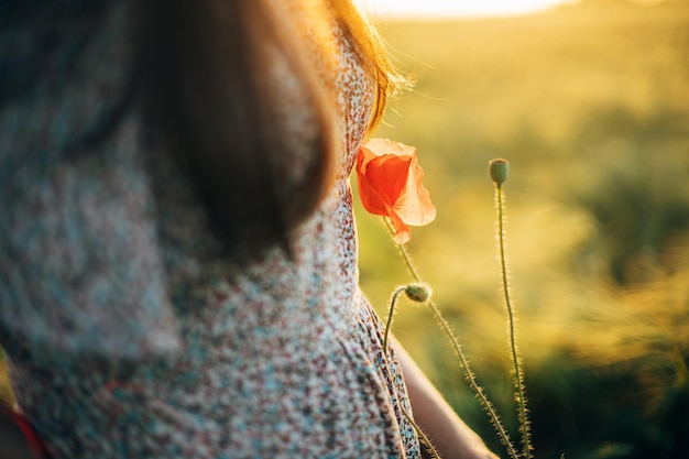 Piękny kwiat maku u kobiety w kwiecistej sukience z bliska na polu jęczmienia w świetle zachodu słońca Stylowa kobieta relaksująca się wieczorem na letniej wsi i zbierająca kwiaty Atmosferyczna spokojna chwila