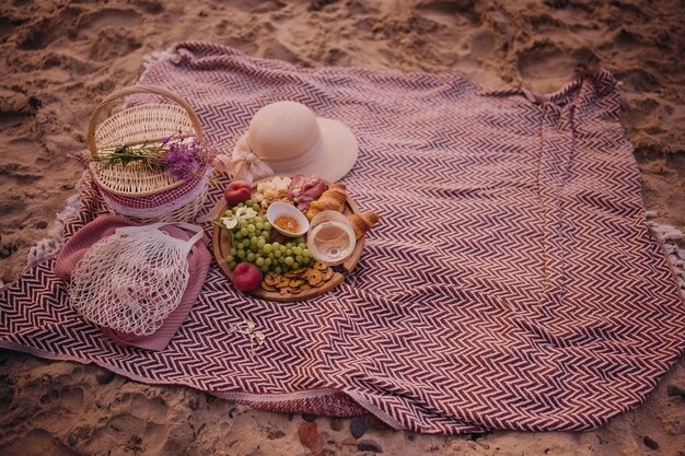 Zdjęcie piękny letni piknik o zachodzie słońca na plaży z białym winem, croissantami, serem i świeżymi owocami.