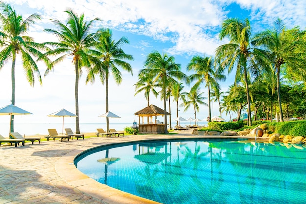 Piękny luksusowy parasol i krzesło wokół odkrytego basenu w hotelu i ośrodku z palmą kokosową na błękitnym niebie - koncepcja wakacji i wakacji