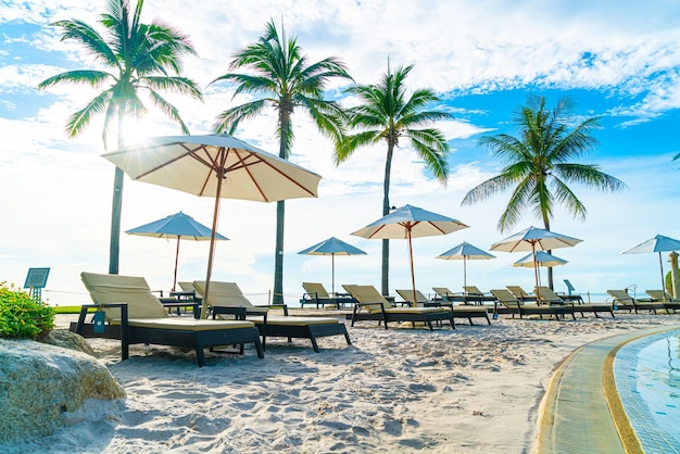 Piękny luksusowy parasol i krzesło wokół odkrytego basenu w hotelu i ośrodku z palmą kokosową na niebie o zachodzie słońca lub wschodzie słońca - koncepcja wakacji i wakacji