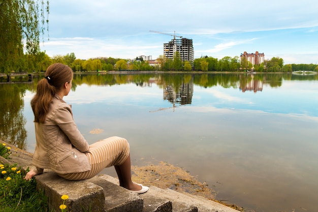 Zdjęcie piękny młodej kobiety obsiadanie na banku duży jezioro