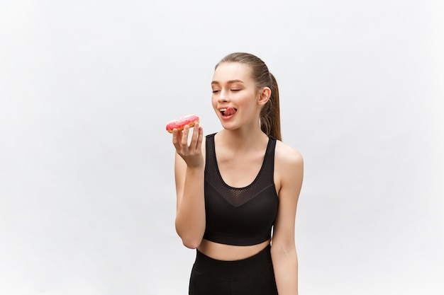 Piękny model fitness na sobie czarny strój fitness, trzymając deser fast foodów.