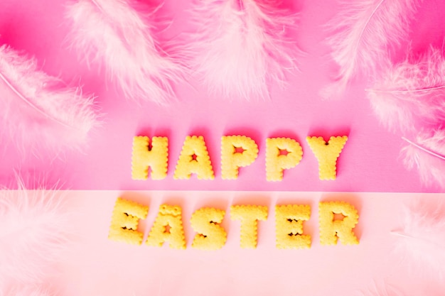 Piękny napis Happy Easter ciasteczka na różowym pastelowym tle z białymi piórami, widok z góry
