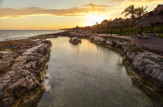 Piękny naturalny basen na skalistym wybrzeżu o zachodzie słońca w Puerto Aventuras w Meksyku.