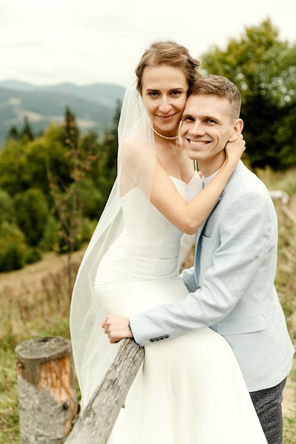 Zdjęcie piękny nowożeńcy przytulają się i uśmiechają będąc w naturze portret młodej pary w koronkowej sukience dzień ślubu szczęśliwej pary para nowożeńców w górach