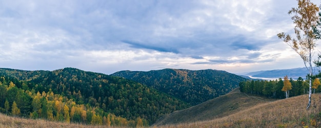 Piękny panoramiczny widok na wzgórza i rzekę na tle ciemnych chmur z zachodzącym słońcem