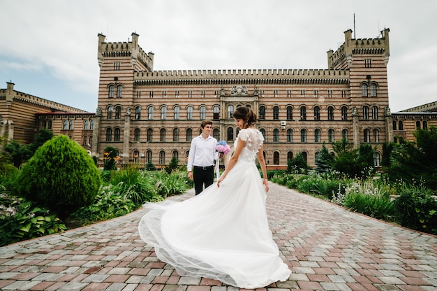 Piękny Portret Panny Młodej Tańczy Dla Pana Młodego I Kręci Się Z Powrotem W Pobliżu Starożytnej Odrestaurowanej Architektury, Starego Budynku, Starego Domu Na Zewnątrz, Zabytkowego Pałacu Na świeżym Powietrzu.