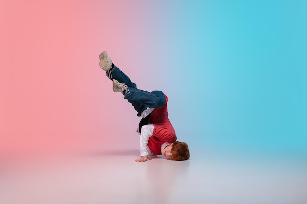 Piękny sportowy chłopiec tańczy hip-hop w stylowe ubrania na kolorowe tło gradientowe w sali tanecznej w świetle neonowym. Kultura młodzieżowa, ruch, styl i moda, akcja. Modny jasny portret.