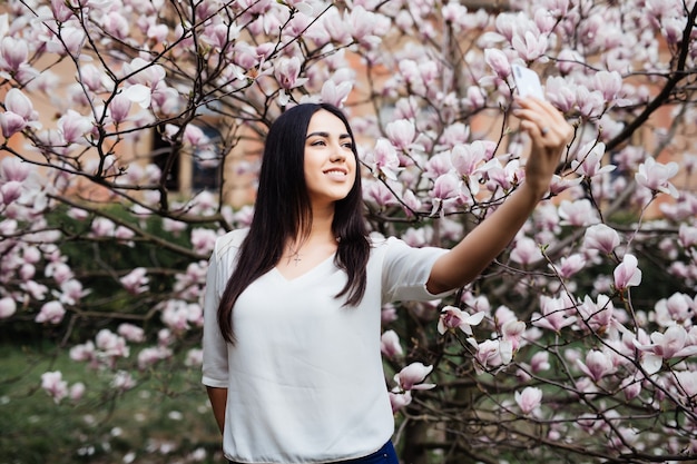 Piękny Stylowy Kaukaski Kobieta Robi Selfie W Ogrodzie Magnolii Kwiat. Wiosna