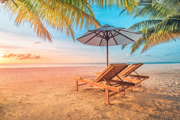 Piękny tropikalny zachód słońca, para leżaków krzesła parasol pod liśćmi palmy. Niesamowita plaża?