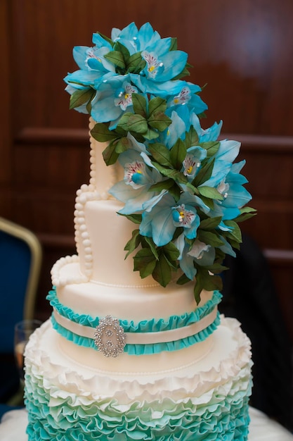 Piękny turkusowy trzypoziomowy tort weselny z kwiatami na wierzchu