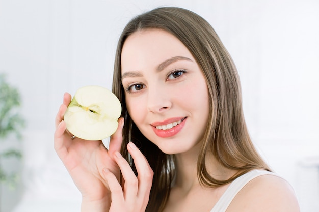 Piękny uśmiech, białe mocne zęby. Głowa i ramiona młodej kobiety z śnieżnobiałym uśmiechem, trzymając zielone jabłko, pielęgnacja zębów.