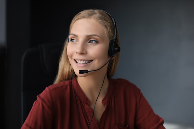 Piękny uśmiechający się pracownik call center w słuchawkach pracuje na białym tle nad szarym tłem.