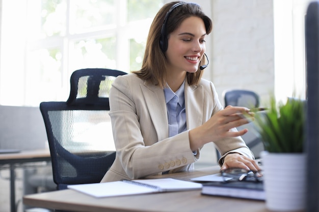 Piękny uśmiechający się pracownik call center w słuchawkach pracuje w nowoczesnym biurze.