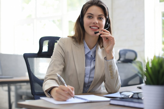 Piękny uśmiechający się pracownik call center w słuchawkach pracuje w nowoczesnym biurze.