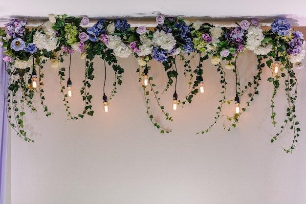 Piękny wystrój z girlandą ze świecącymi lampami i dekoracjami kwiatowymi Dekoracja z kwiatów na ceremonię ślubnąxA