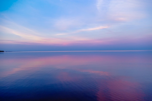 Piękny zachód słońca nad morzem, pastelowe kolory i refleksy na wodzie, spokojny krajobraz z kolorowymi chmurami i morzem. Naturalny gradient środowiska. Abstrakcyjne tło.