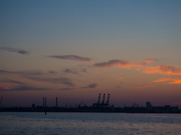 Piękny zachód słońca nad portem z sylwetkami dźwigów towarowych Przemysłowy port czarnomorski Odessa Ukraina z dużą ilością dźwigów Kabiny i zbiorniki nad wodą o wieczornym zmierzchu