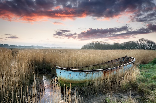 Piękny zachód słońca nad starą zardzewiałą łodzią rybacką wyrzuconą w trzciny na brzegach Poole Harbor w Dorset