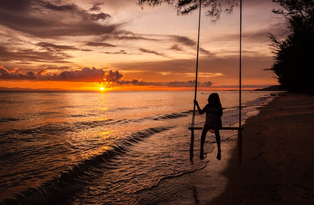 Piękny zachód słońca tropikalna plaża, dziewczyna jest szczęściem kołysząc się na huśtawce.