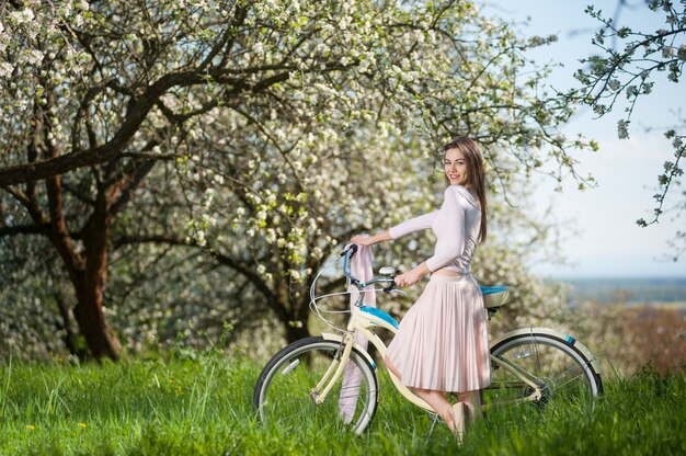 Piękny żeński cyklista z retro bicyklem w wiosna ogródzie