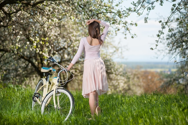Piękny żeński cyklista z retro bicyklem w wiosna ogródzie