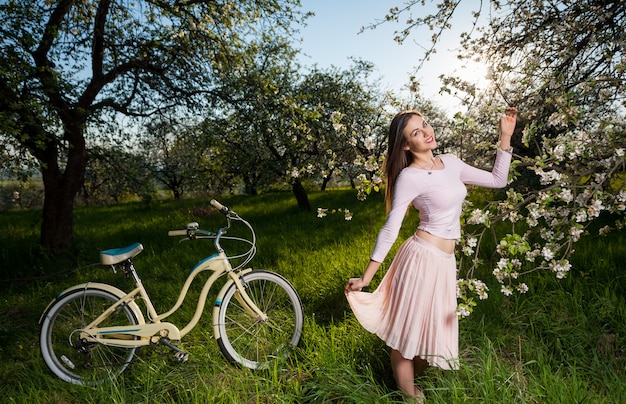 Piękny żeński cyklista z retro bicyklem w wiosna ogródzie