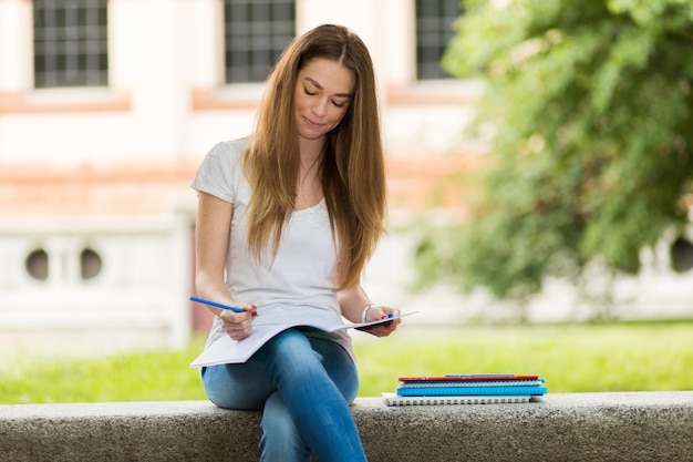 Piękny żeński student collegu czyta książkę na ławce w parku