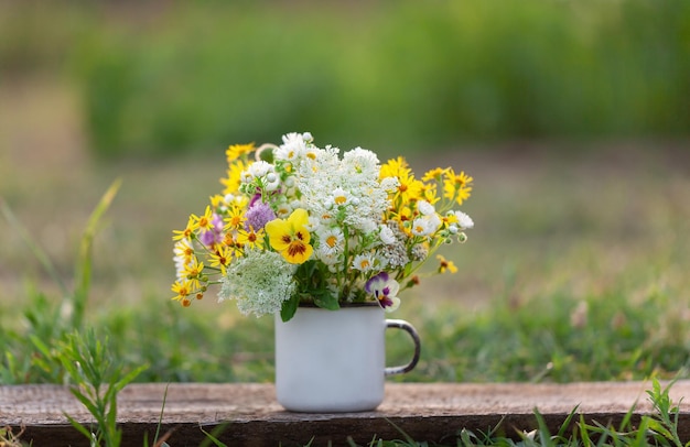 Piękny żółty bukiet dzikich kwiatów w białej filiżance na drewnianym stole i tle przyrody. Koncepcja lato.