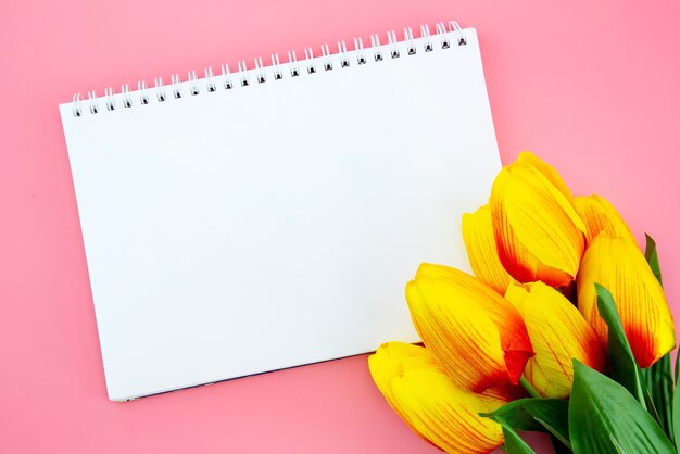 Zdjęcie piękny żółty tulipanowy kwiat i papier na różowym tle