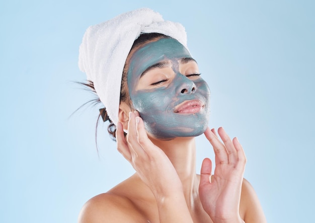 Pielęgnacja ciała wellness i maska na twarz z węglem drzewnym dla zdrowej skóry kobiety na niebieskim tle studia makiety Młody szczęśliwy i piękny model kosmetyczny z produktem przeciwstarzeniowym dla dobrego samopoczucia i pielęgnacji