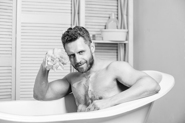 Pielęgnacja i pielęgnacja Przystojny muskularny mężczyzna relaksująca wanna Koncepcja ciepłej kąpieli Przekształć swoją łazienkę we własne prywatne spa Macho z gąbką wykąp się w domu Kąpiel z mydlinami