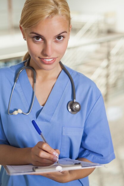 Zdjęcie pielęgniarka pisze w schowku podczas gdy patrzejący kamerę