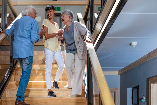 Pielęgniarka pomaga roześmianym seniorom na schodach