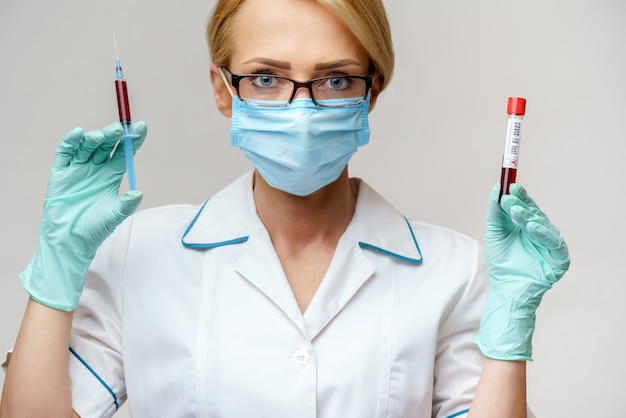 pielęgniarka w masce ochronnej, trzymając strzykawkę i probówkę z krwią