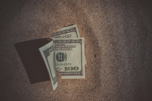 Pieniądze dolary do połowy pokryte piaskiem leżą na zbliżeniu plaży