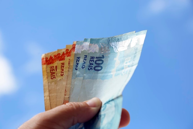 Pieniądze z brazylii trzymającej brazylijskie prawdziwe banknoty z niebem w tle