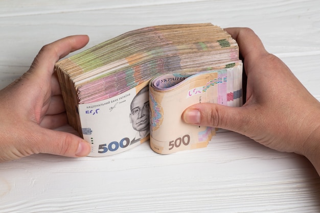 Pieniądze z Ukrainy. Stos banknotów hrywny ukraińskiej w ręce na drewnianym stole. Hrywna 500 i 200 hrywien