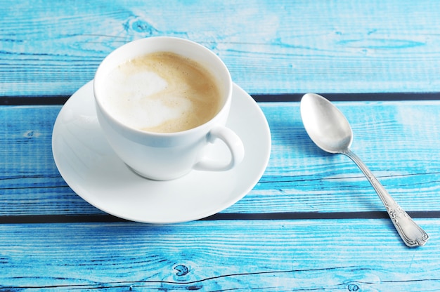 Pienista kawa z cappuccino w białym kubku na niebieskim tle