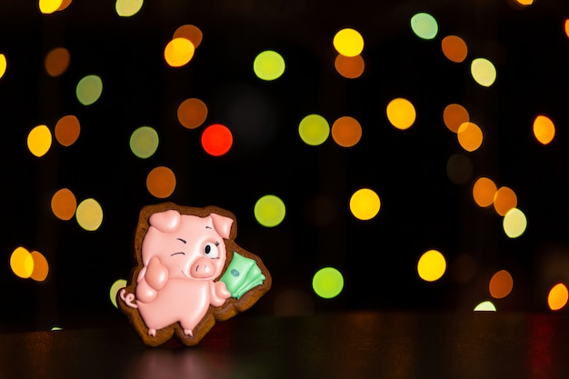 Piernikowe ciastko z zabawną różową świnią od mema przechowuje pieniądze na niewyraźne kolorowe światła girlandy.