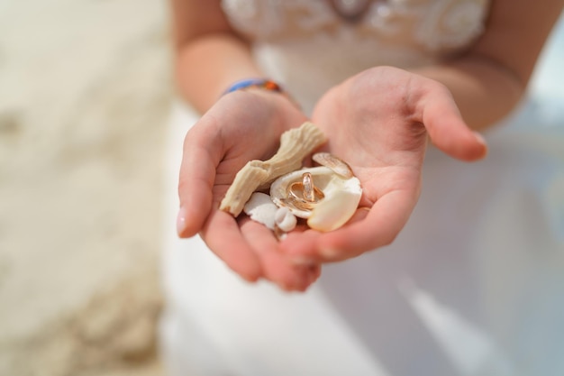 Zdjęcie pierścienie ślubne i muszle w rękach dziewczyny w białej sukience