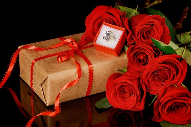 Pierścionek w czerwonym pudełku i piękne czerwone róże na czarnym tle. Koncepcja Walentynki.