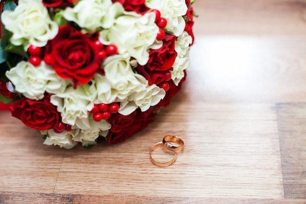 Pierścionki i ślubny bukiet czerwonych i białych róż na stole