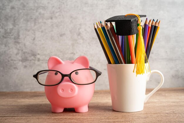 Pigging bank noszący okulary z kolorowymi ołówkami oszczędzający koncepcję edukacji bankowej